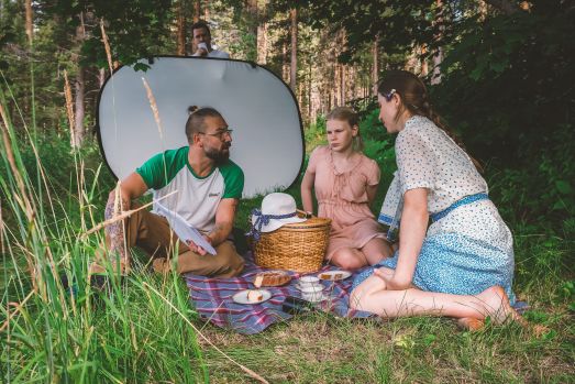 Marcel Köppe sitter i gräset och pratar med ett par skådespelare.