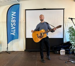 Jonas står på en inomhusscen och spelar på en gitarr.